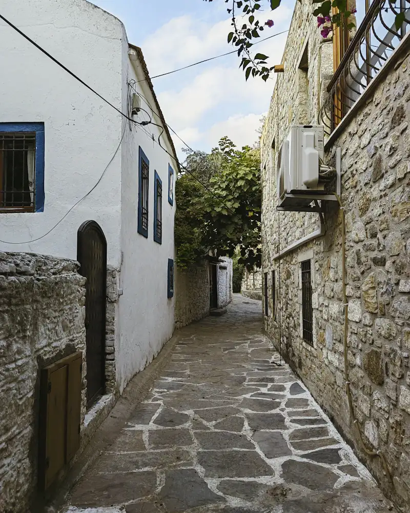 Bir yanı beyaz badanalı, bir yanı taş duvarlı, taş döşeli dar bir sokak.